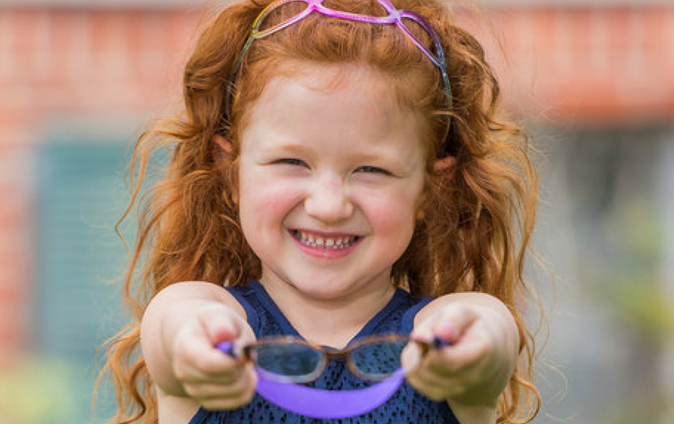 Little girl with red hair holding up glasses