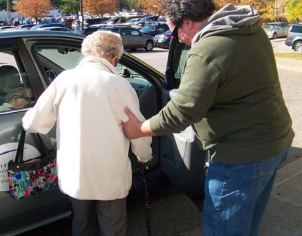 A man helping an older woman into a car